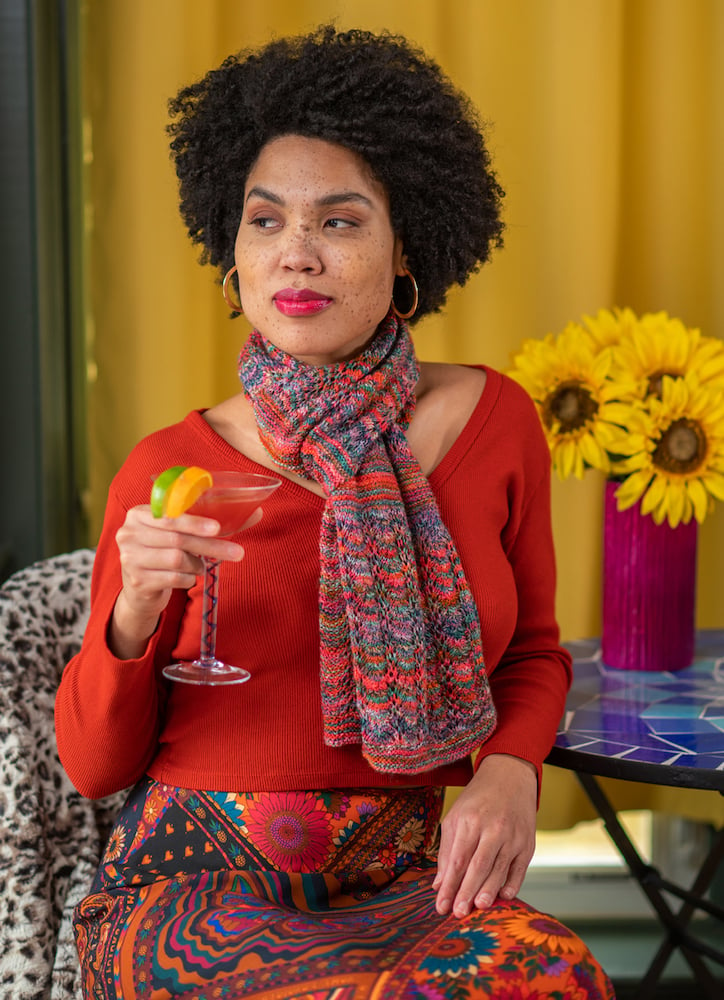 Photo of talent in hand-knit scarf smiling with Cosmopolitan cocktail glass in hand, in front of colorful background with sunflowers, by Branford, Connecticut-based fashion photographer Gale Zucker. 