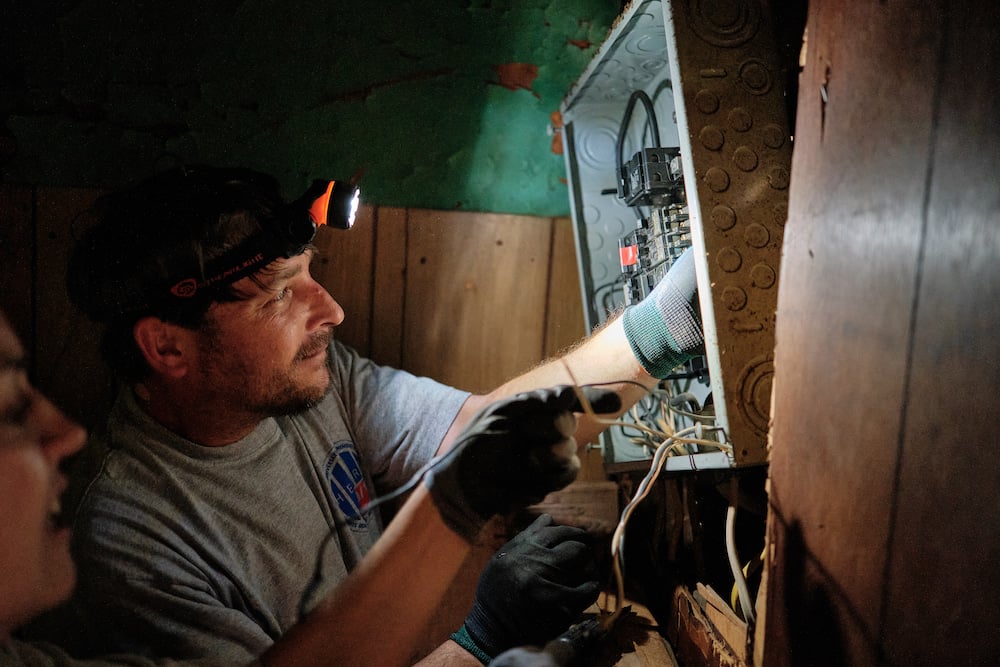Image two volunteers rewiring electrical box, using headlamps, by Mobile, Alabama-based conflict/crisis and humanitarian photographer Dan Anderson. 