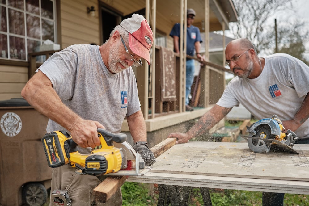 Photo of two volunteers ripping plywood sheathing with circular saws, outdoors on sawhorses, by Mobile, Alabama-based conflict/crisis and humanitarian photographer Dan Anderson. 