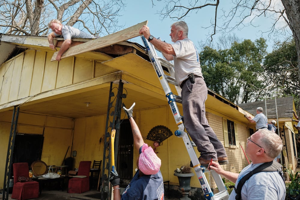 Photo of four volunteers installing new wood flashing on roof, by Mobile, Alabama-based conflict/crisis and humanitarian photographer Dan Anderson.