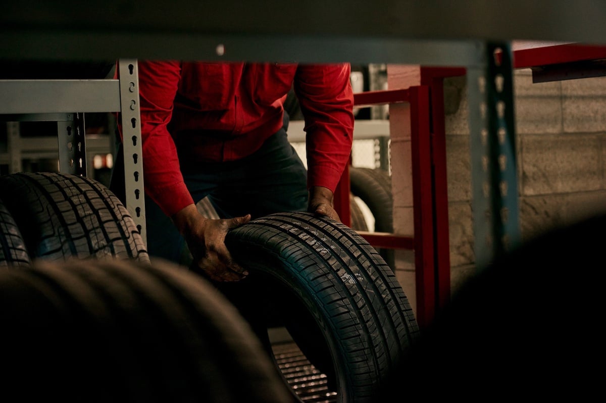 Photo of Belle Tire employee in red uniform, lifting tire in mechanic's shop, by Chicago-based brand narrative photographer Nathanael Filbert.