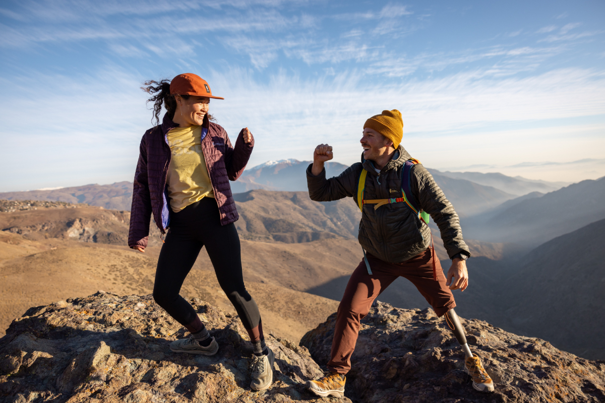 A color photo by Adam Wells of two models at the summit of a mountain preparing to fist-bump.