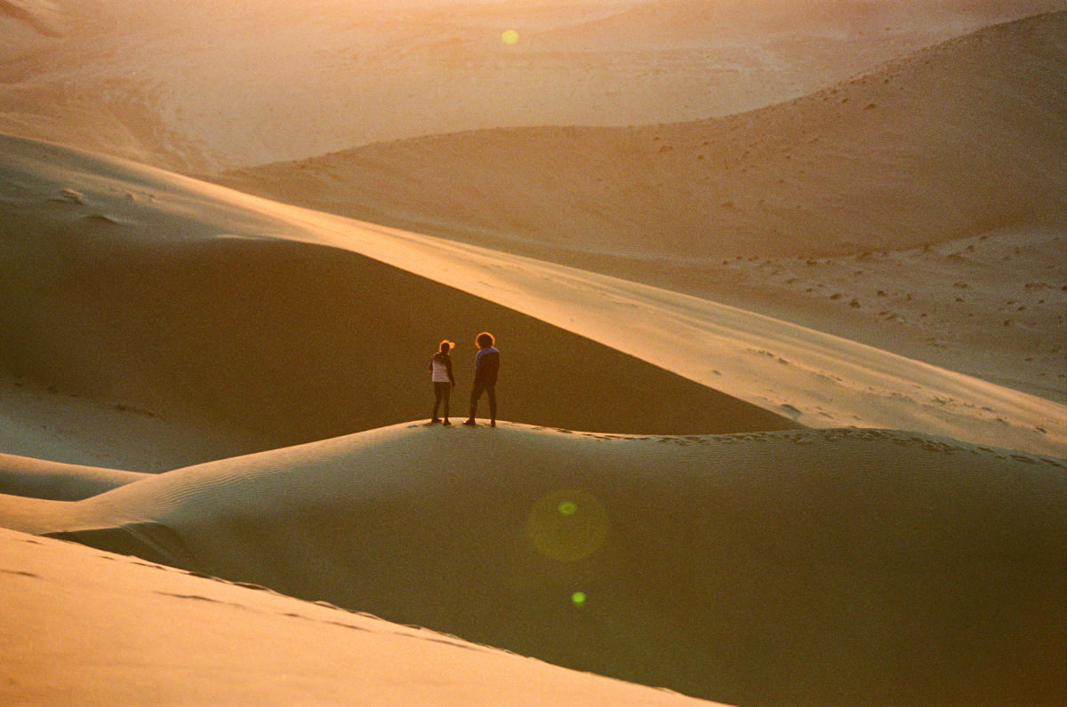 A color photo by Adam Wells of two models in the sand dunes.