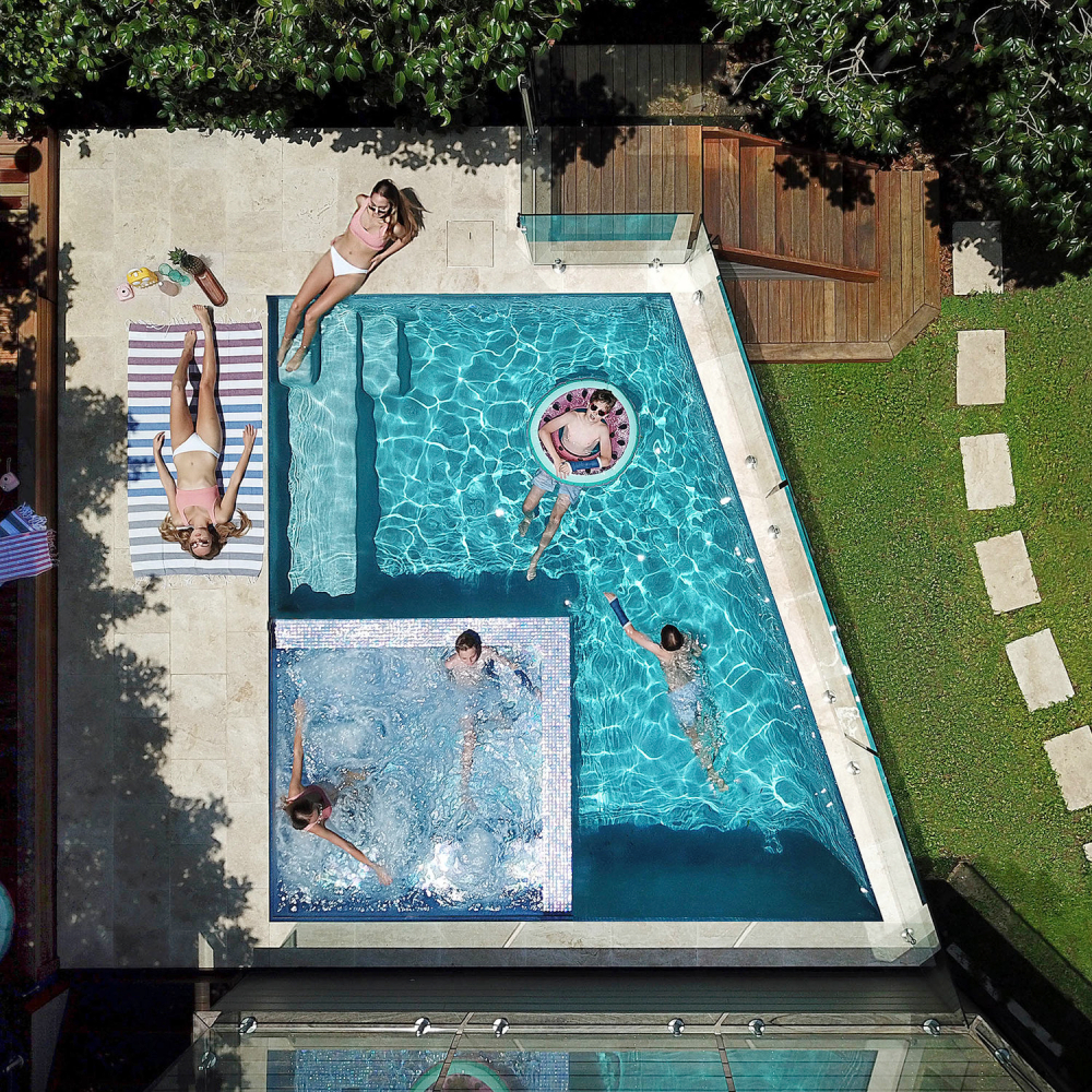 Photo by Andrew D. Richardson of a backyard swimming pool with kids and adults swimming and sunbathing.