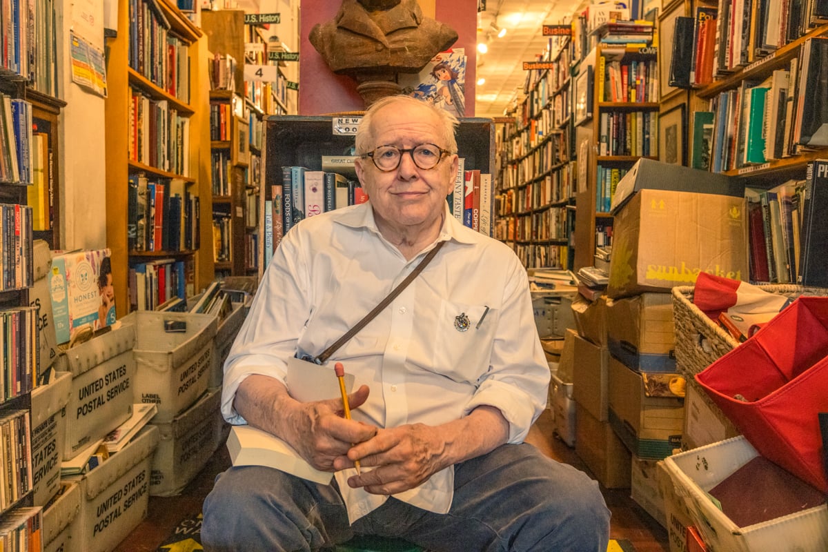 A photo by Zave Smith of a bookstore owner surrounded by books in his store.