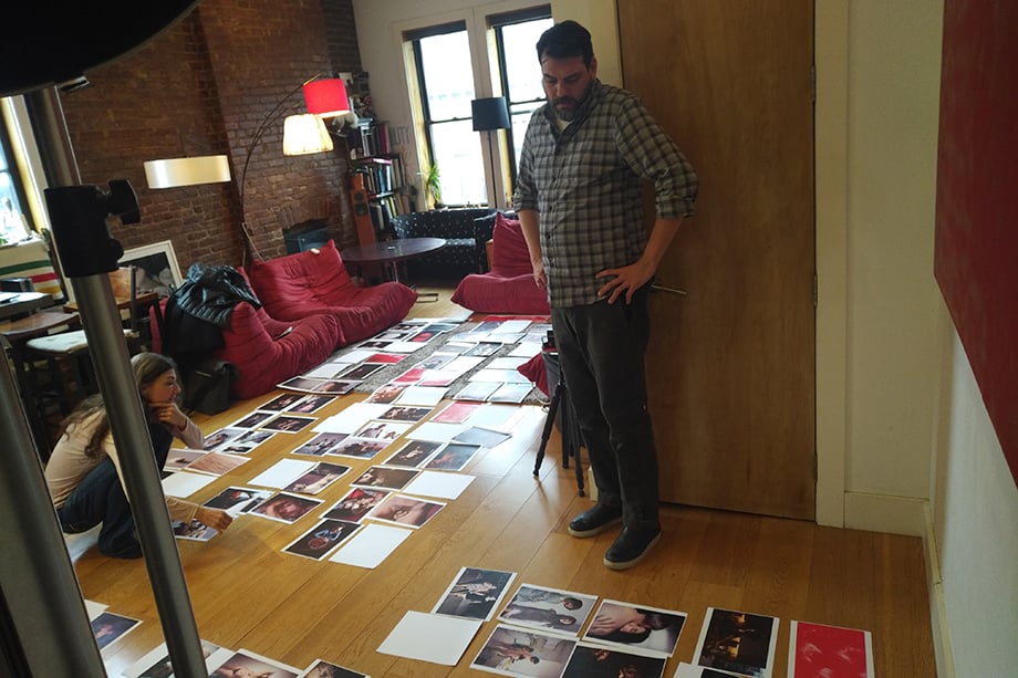A behind the scenes image capturing Elinor and Alan surrounded by printed pages of photos, sequencing them for her photobook.