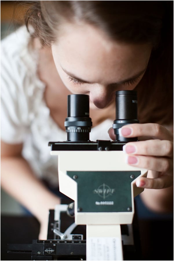 A young woman looks into a microscope by photographer Gregory mILLER