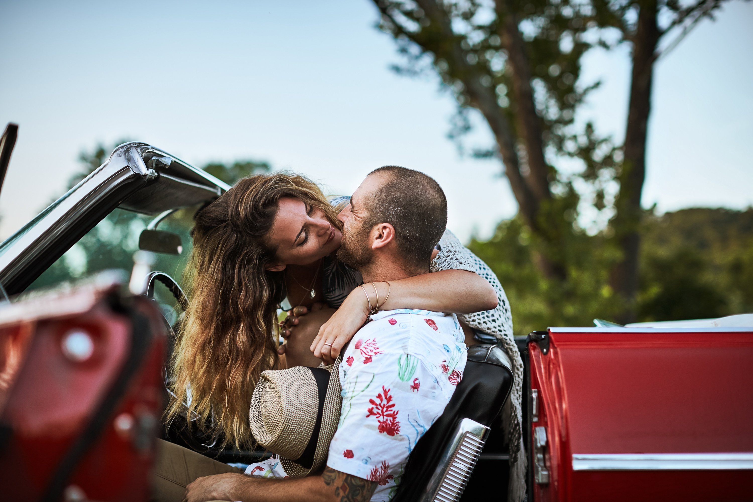 A woman leans over a man in the front seat of the car to give him a kiss in this shot by Jay Fram 