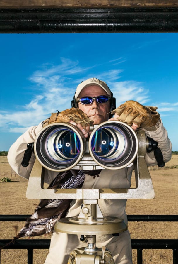 A man poses with big binoculars on a ranch by photographer Jeff Wilson of Austin Texas 