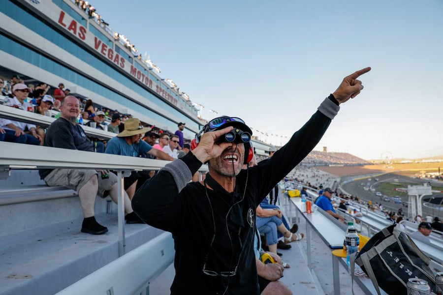 A man cheers as he looks through binoculars at the Las Vegas Motor Dervy by photographer Joe Buglewicz