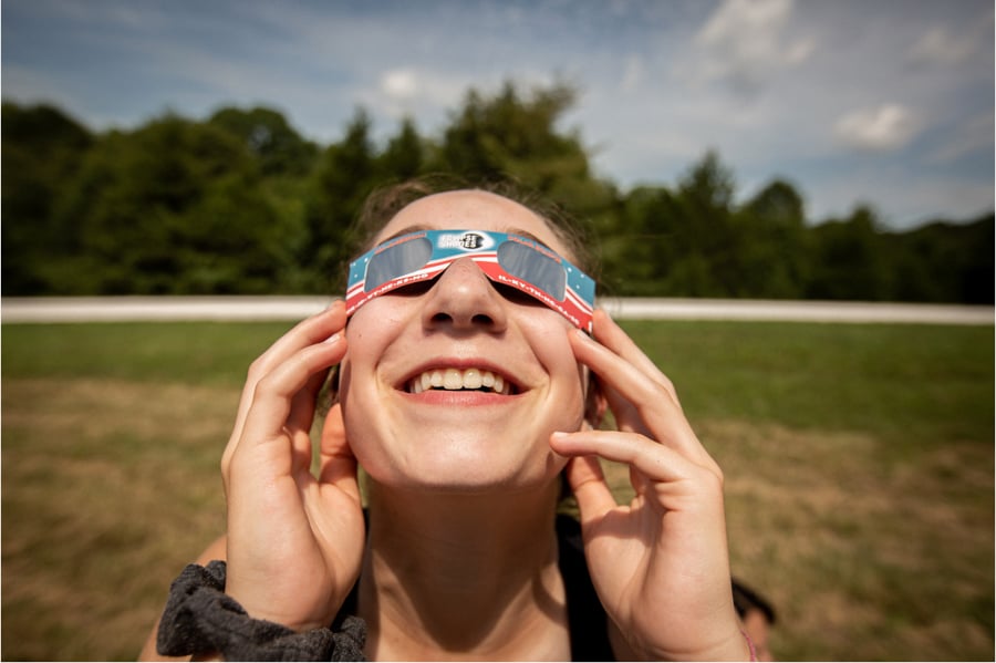 A young person looks up at the sky in cardboard solar eclipse glasses by Lou Bopp of St. Louis, Missouri