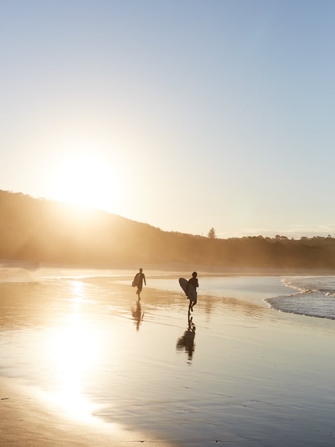 Two silhouetted surfers walking along the shore at sunset by photographer Peter Tarasiuk of Melbourne, Australia. 