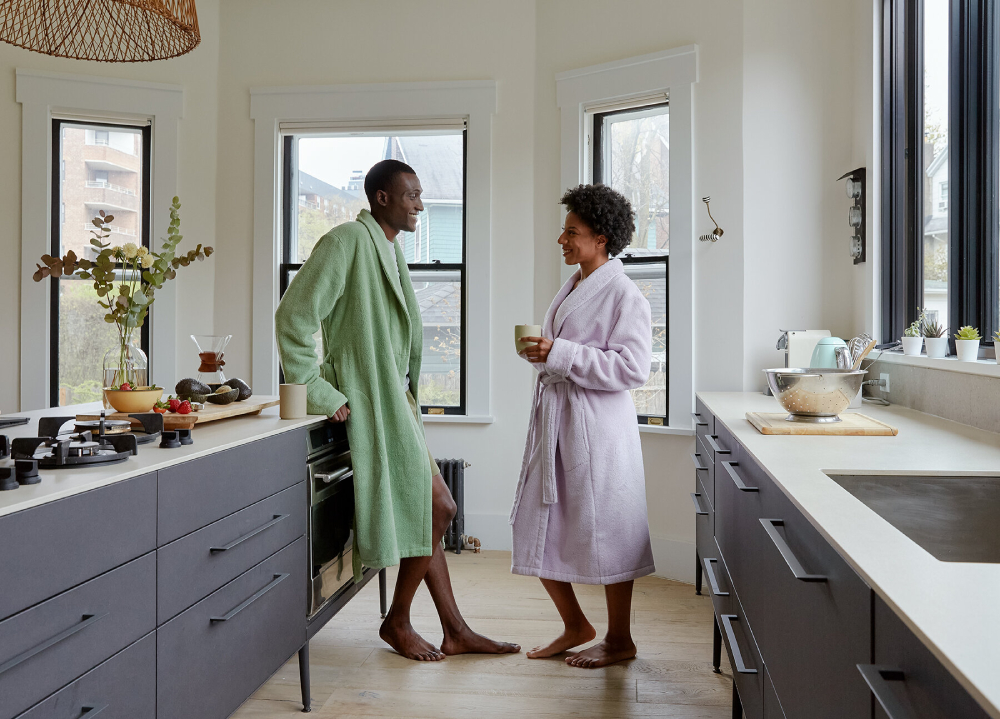 A color photo by Amanda Villarosa depicting two people wearing bathrobes happily talking while drinking their morning coffee in the kitchen.