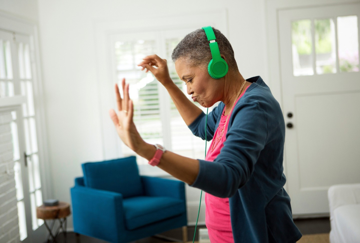 A color photograph by Amy Mikler of a woman with headphones on dancing in her living room.