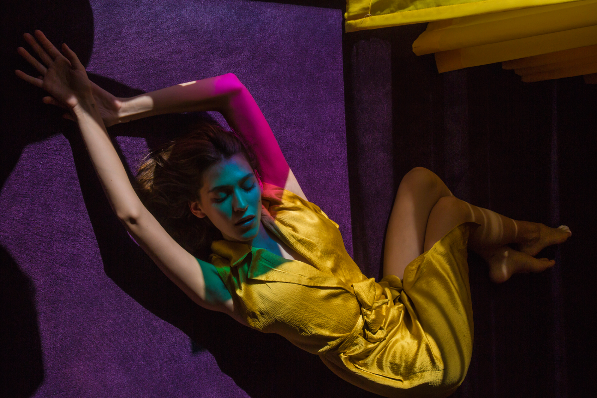 A color photograph by Anna Alexia Basile of a woman reclining on purple stairs under pink and blue filtered light.