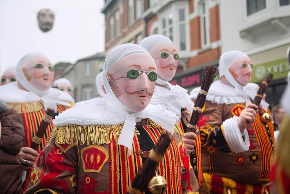 Masked gilles with their bundles of twigs march through the city of binche