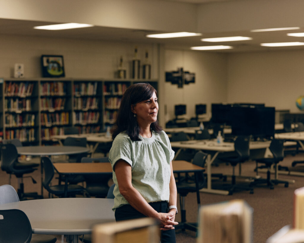  portrait of Maile Steimer, a media specialist at Gwinnett's Jones Middle School, taken in a library setting. With her hands gracefully crossed in front of her, she emanates an aura of contemplation and composure, captured by the lens of Ben Rollins.