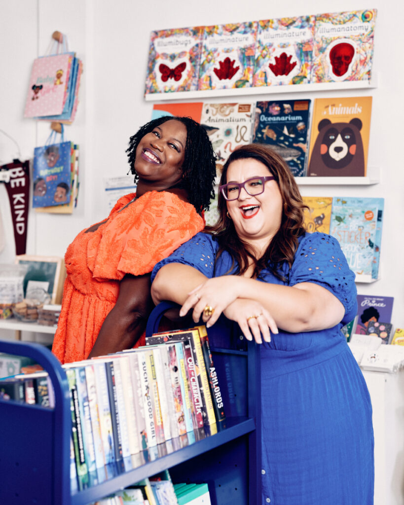 A delightful portrait captured in a library, featuring two young adult book influencers, Kimberly Jones and Vania Stoyanova. Their smiles radiate warmth and enthusiasm, reflecting their passion for literature and shared joy in the moment.