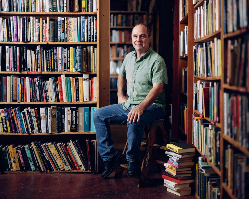 This portrait showcases Frank Reiss, the owner of A Cappella Books, immersed in a sea of literature within the confines of library. 