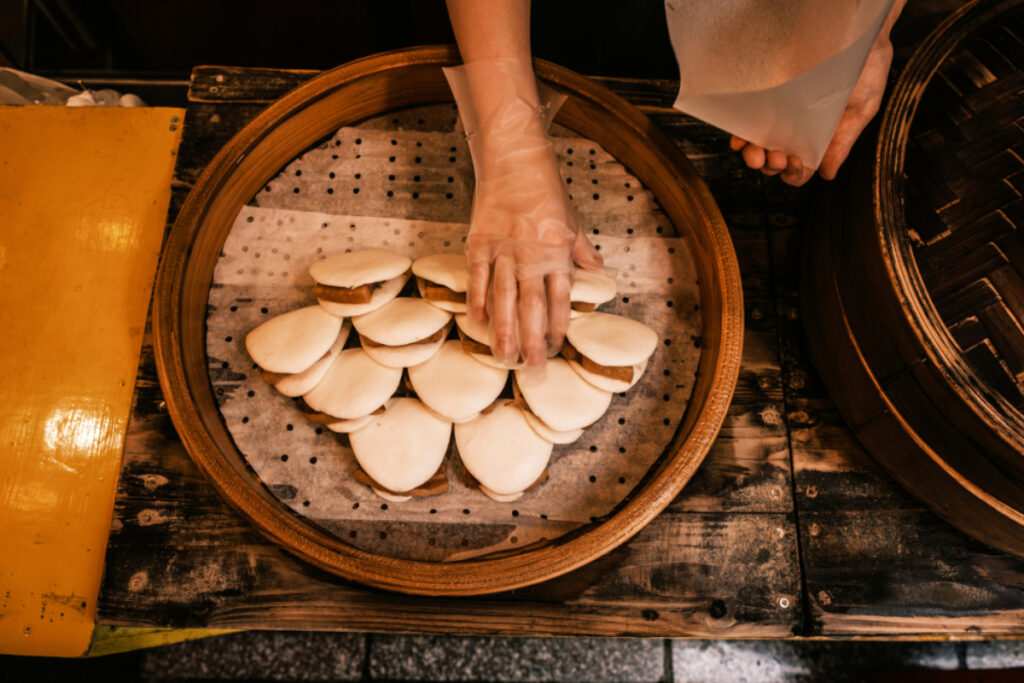 A cook meticulously stacks fluffy bao buns atop a bamboo steamer, showcasing the artistry and precision involved in crafting these delectable culinary delights.