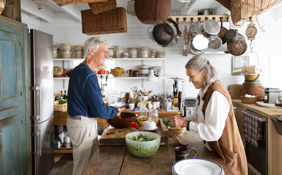 A color photograph by Buff Strickland of elderly couple cooking in their rustic kitchen. 