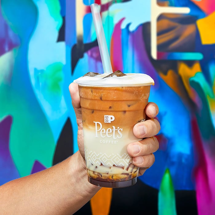 Man holding Peet's iced cofee in front of colorful background.