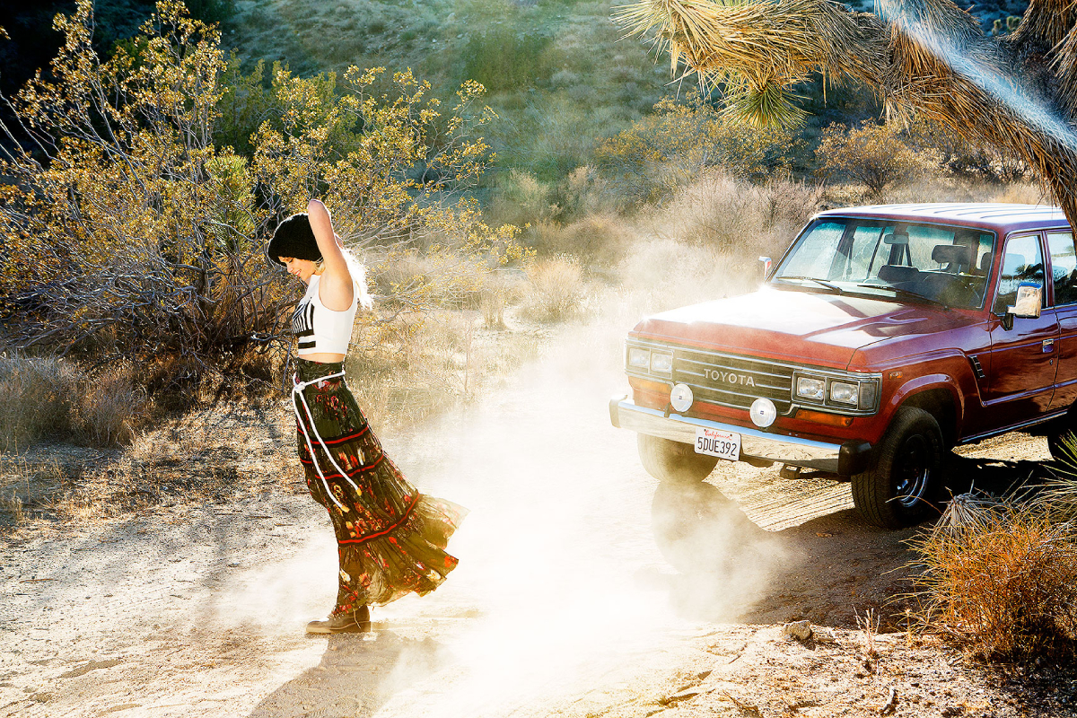 An image by one of our premier Fashion photographers in San Francisco, Cheyenne Elis shows a woman standing in front of a Toyota truck as a gust of wind blows dust into the sunlight behind her. 
