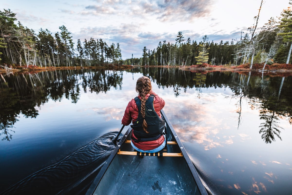 A lifestyle landscape photo of a woman paddling a canoe by Chris Bennett.
