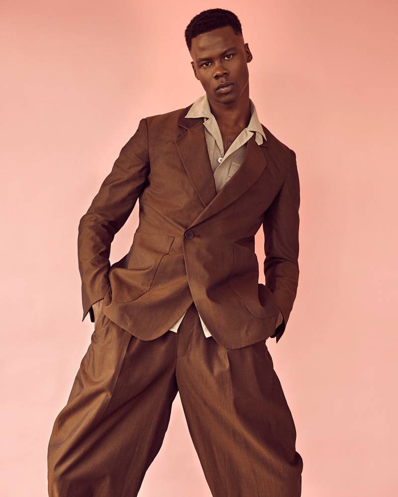 A photo by Christopher Morris of a man wearing a brown suit against a peach colored background.