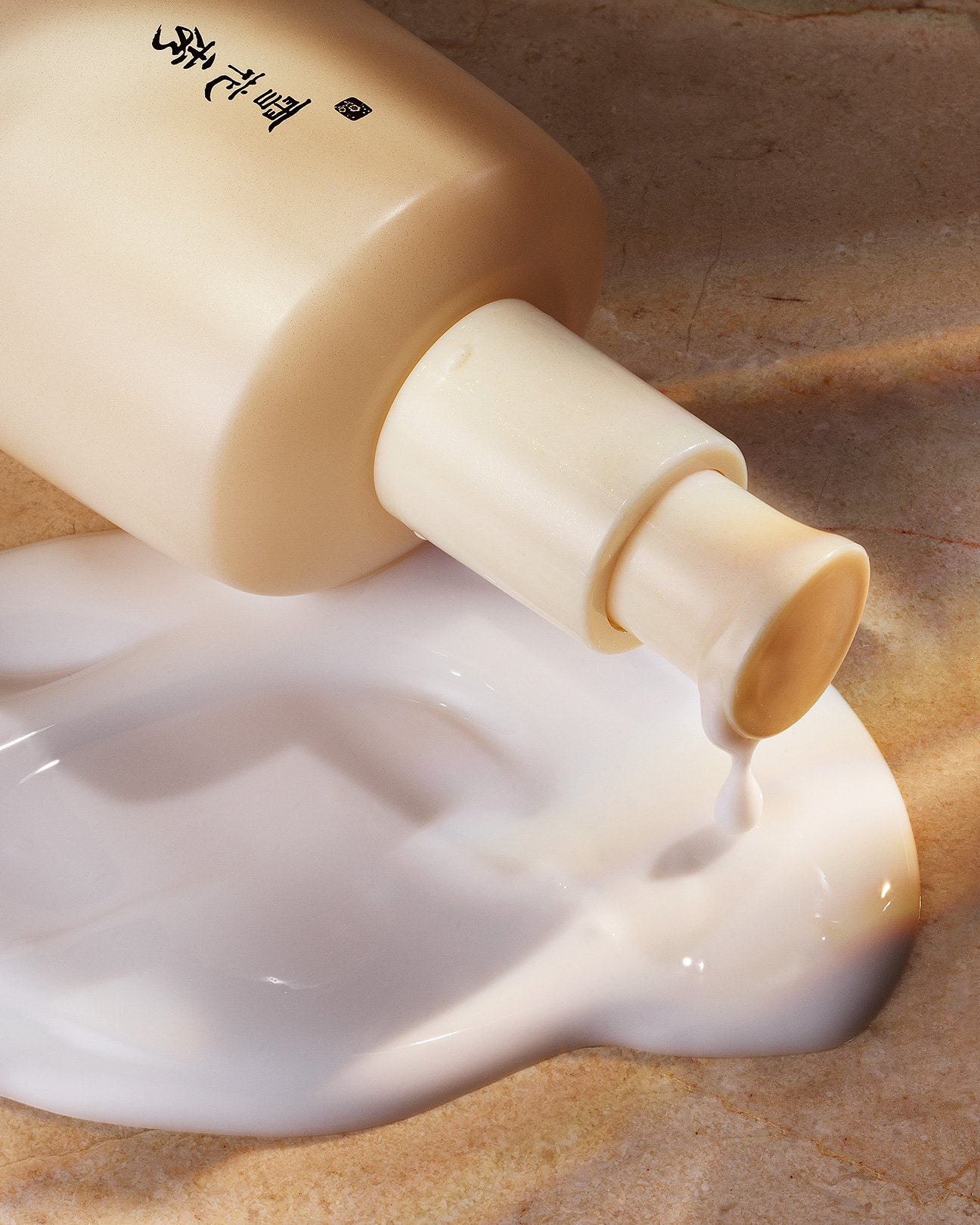 A color photograph by Clair Benoist of a bottle laying on its side with lotion slowly spilling out.
