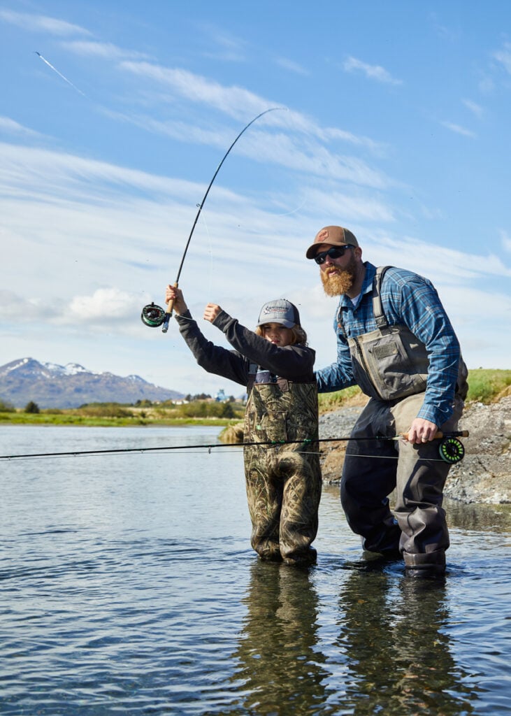 A color photo of a boy and a man fly fishing by Clay Cook.