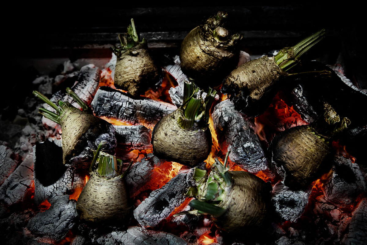 A color photo by Dean Cambray of celery roots roasting directly on wooden coals.