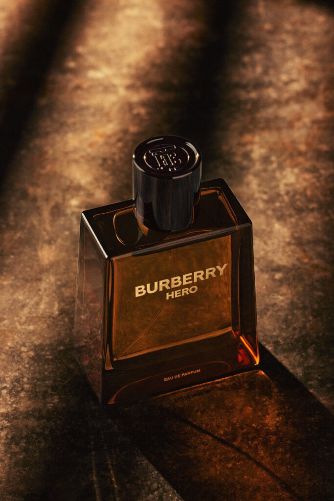 Jeremy Kramer's photo of a bottle of Burberry Hero perfume. The bottle is made of transparent brown glass and says Burberry Hero in gold. The bottle is trapezoidal in shape- slightly wider at the base than the top. 