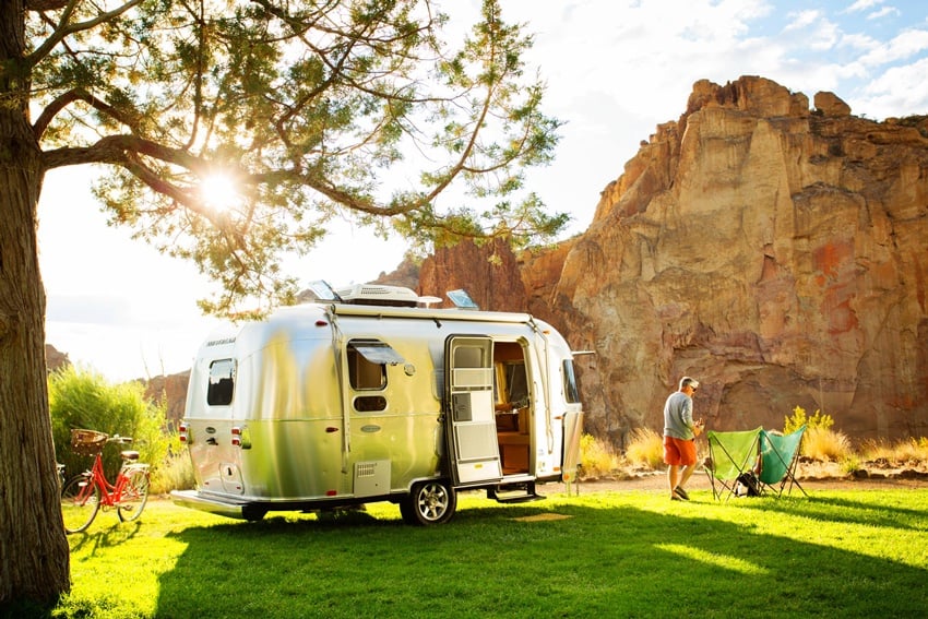 Jim Henderson's photo of an old-fashioned style silver trailer parked on grass and under a tree, in front of an outcropping of red rock.