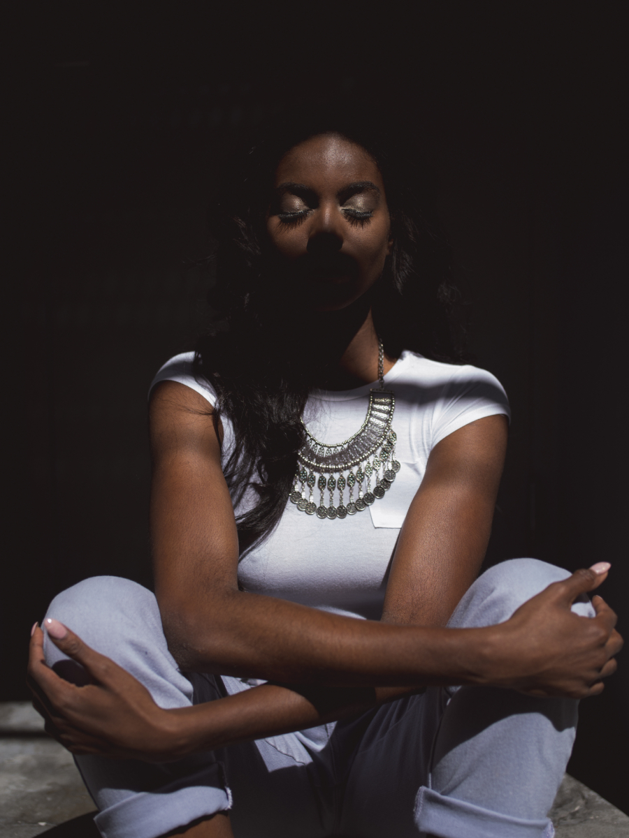 A color photo by JJ Casas of a woman sitting with eyes closed under a pattern of shadows.