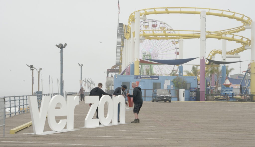 A BTS image of the Verizon logo on the Santa Monica Pier with a rollercoaster in the background