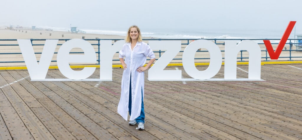A photo by John David of a woman posing in front of the Verizon letters on the Santa Monica pier.