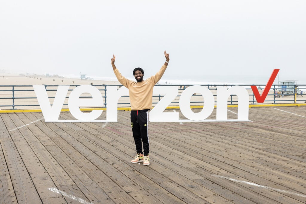 A photo of a man posing in front of the Verizon letters on the Santa Monica pier.