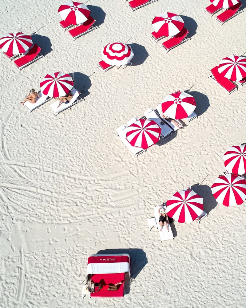 Aerial photo by John Olive of a beach  with people relaxing under many red and white umbrellas.