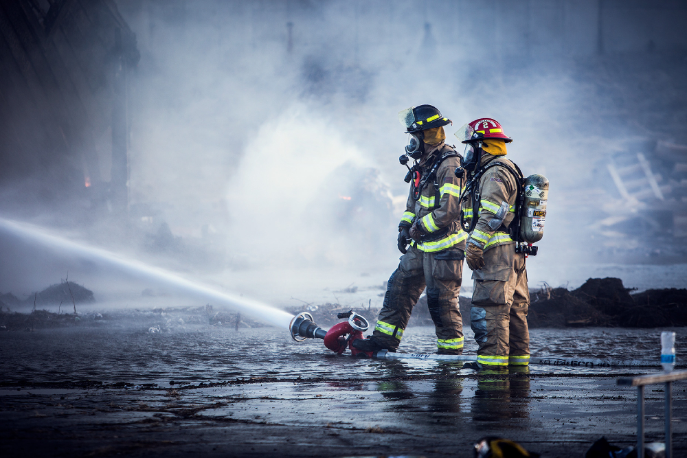 Photo by John Sibilski of two firefighters aiming a firehose within a disaster setting.