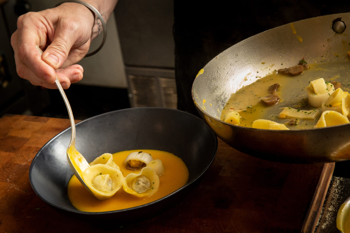 A color photo by Portland Food photographer John Valls of a man placing tortellinis from a pan into a bowl with sauce.