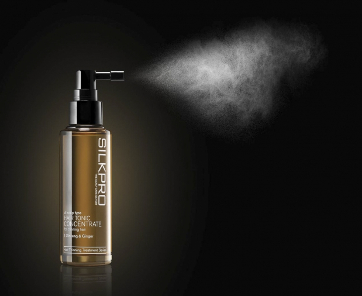 A captivating image captures the Silkpro Hair Tonic Concentrate as it gracefully releases its revitalizing elements into the air, creating a mist against a sleek black background, photo by a Singapore product photographer Johna Sue.