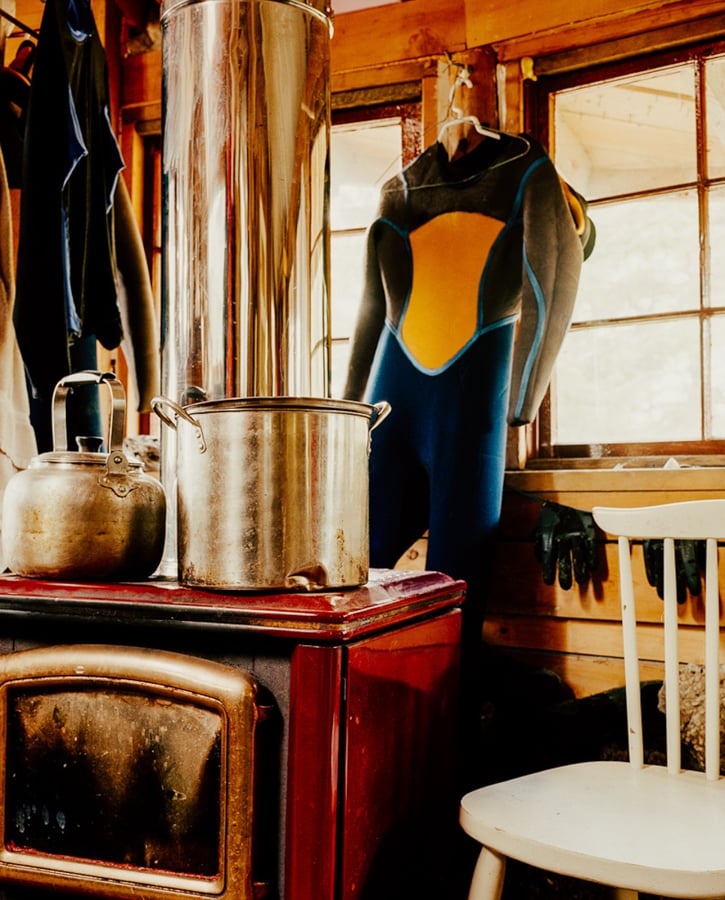 Wet suits hanging behinf an old stove in a cozy surf shack by photographer Kamil Mialous of Vancouver, Canada