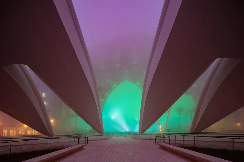 A color photo washed in fog and neon purple and green light of a large and seemingly futuristic building by Katarina Premfors.