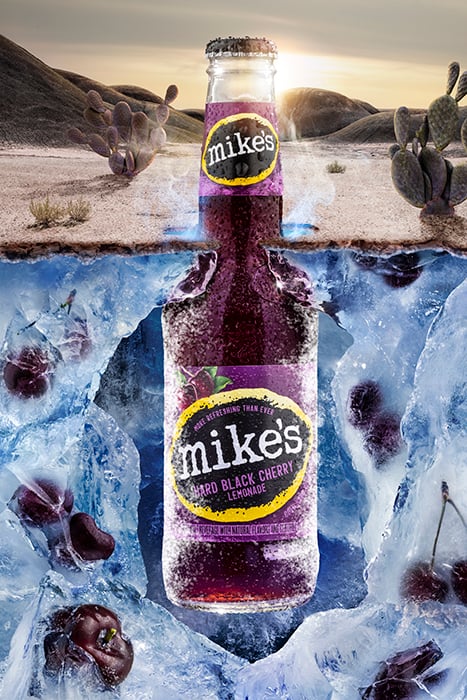 a bottle of Mike's Hard Black Cherry Lemonade emerges from the icy underground, the background a desert during sunrise 