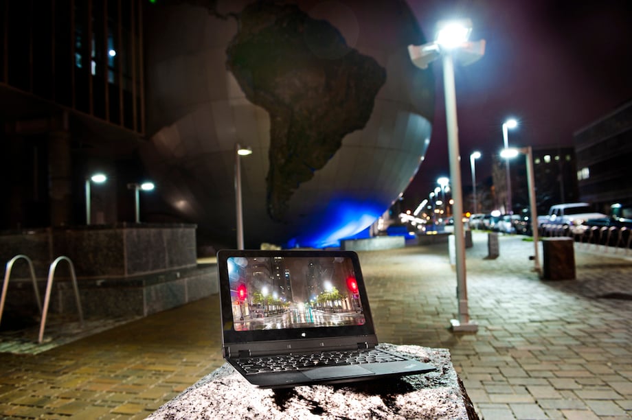 A Lenovo laptop with a screensaver of a well-lit street, positioned on a bench in the morning 