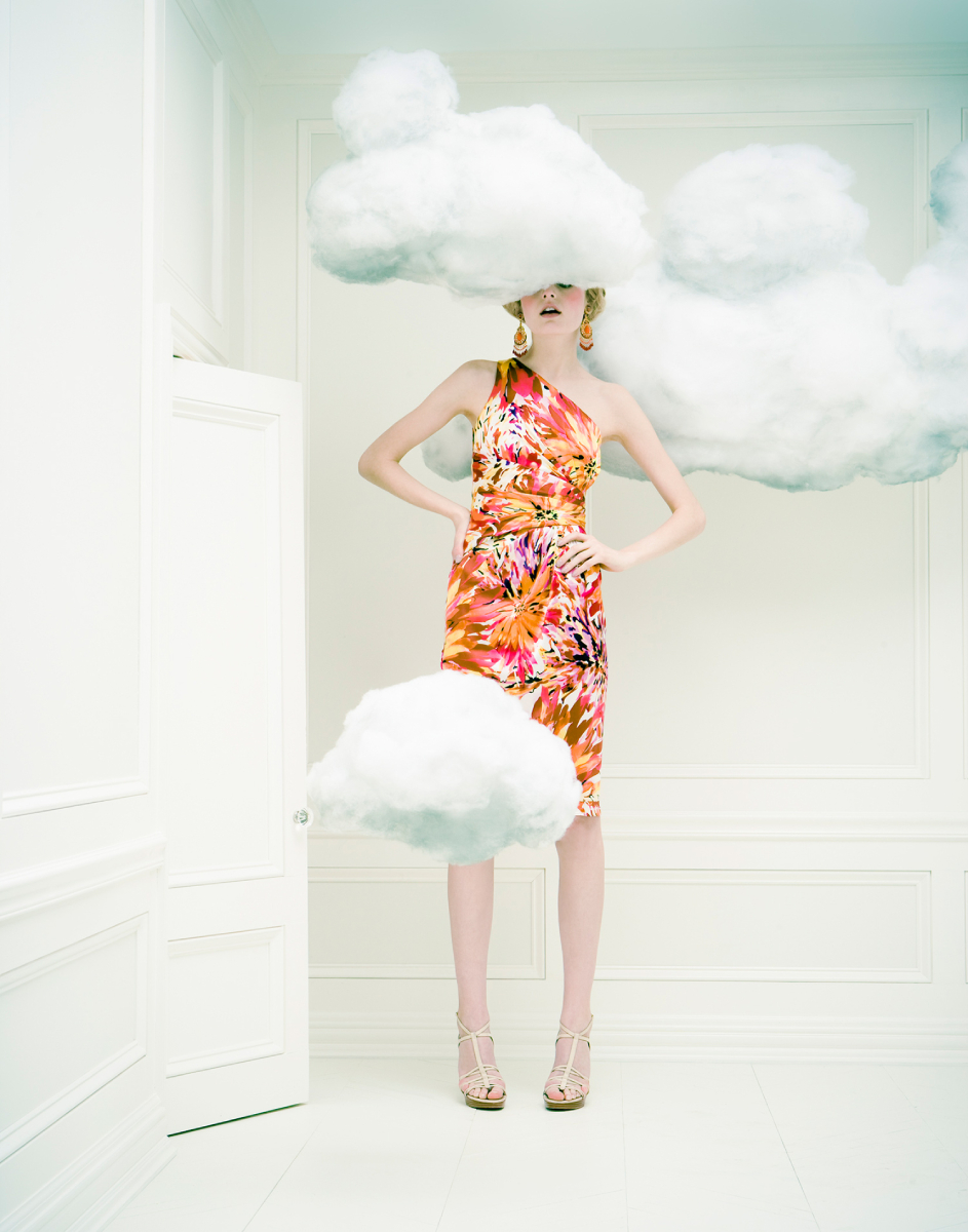 A woman wearing a vibrant knee-length dress enveloped a dreamy ambiance. The white set, adorned with clouds strategically covering parts of her head and body, adds an enchanting and imaginative touch to the overall composition, photo by Atlanta fashion photographer Liz Von Hoene.