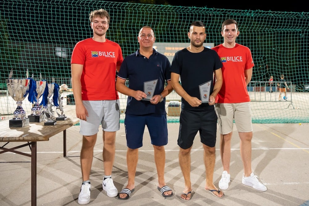 Portrait of brothers, Luka (outer left) and Mate (outer right) in red teeshirts presenting trophies to the tournament's two referees.