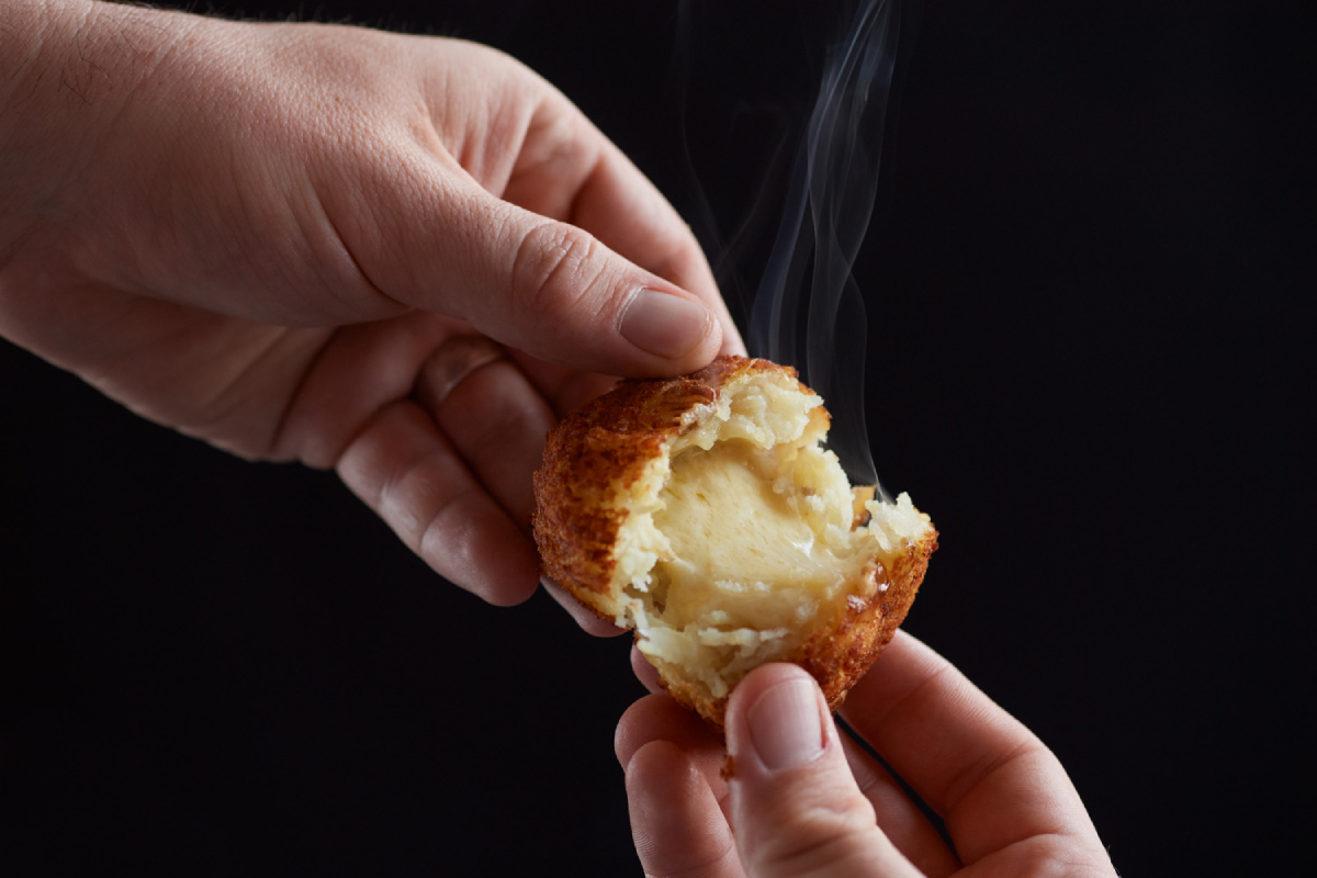 A color photo by Michael Shay of a man's hands breaking open a croquette and steam rising. 