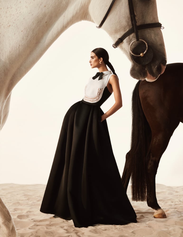 Photo by Nima Benati of a woman standing in classical dress between two horses.